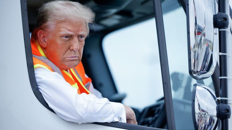 Donald Trump sitting in a garbage truck wearing an orange vest