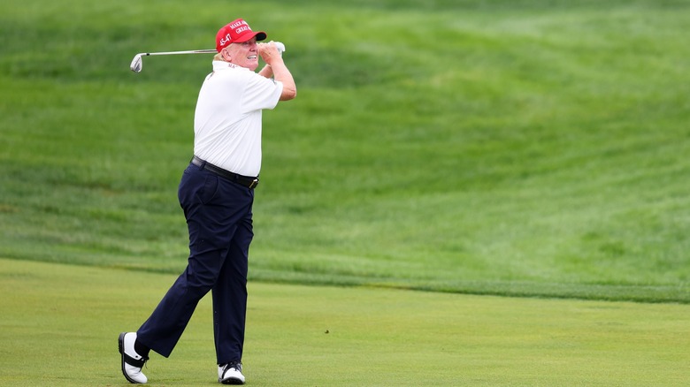 Trump mid-golf swing, wearing a MAGA hat