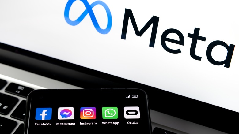 laptop screen with Meta's logo with a cell phone next to it with Facebook, Messenger, WhatsApp, and Oculus apps displayed