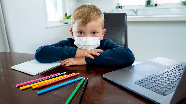 little boy in mask at desk 