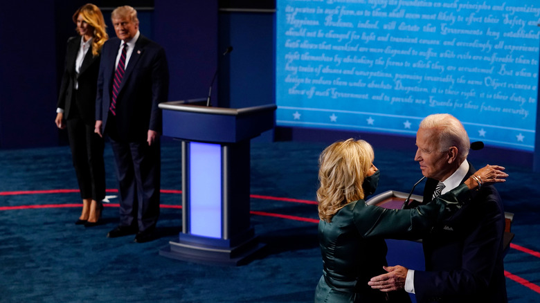 Donald and Melania Trump in the background while Jill and Joe Biden hug