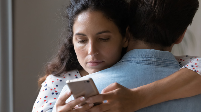 Woman looking at the phone while hugging her partner