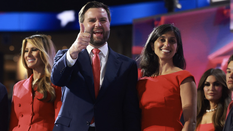 J.D. Vance holding a thumbs up next to Usha Vance and Melania Trump on stage at 2024 RNC