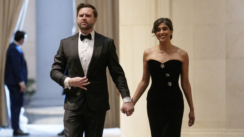 J.D. Vance and Usha Vance walking hand in hand, J.D. in a tuxedo, and Usha in a long black gown.