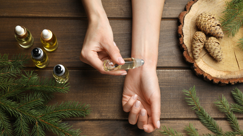 applying perfume to wrist against wood and pine cone background