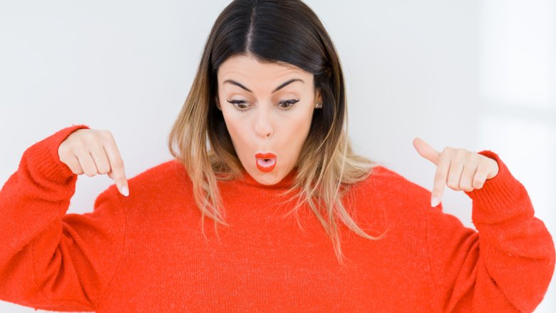 young woman looking surprised and pointing down