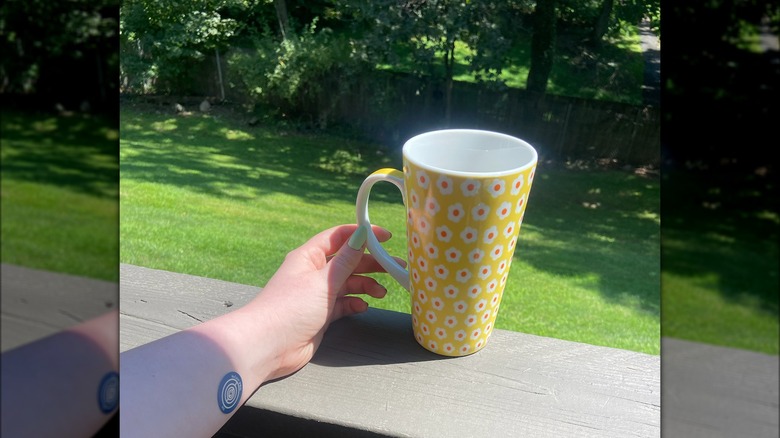 Hand wearing  NuCalm disc with cup of coffee