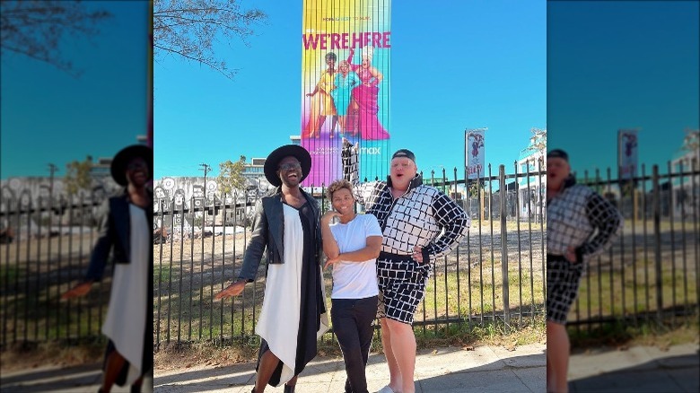 The stars of We're Here pose in front of a billboard