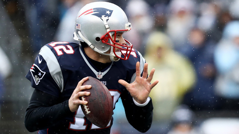 Tom Brady in New England Patriots uniform holding football while snow falls