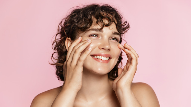 A woman smiling and touching her face 