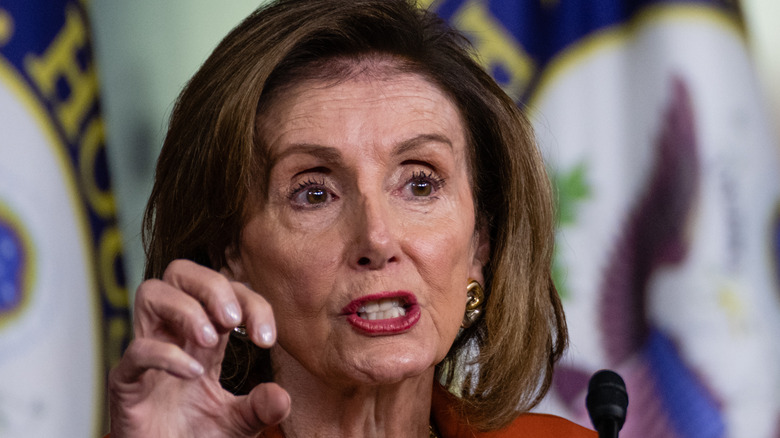 Democratic House Speaker Nancy Pelosi speaking at a microphone looking serious