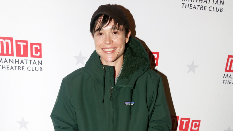 Elliot Page smiling in a green sweatshirt and brown beanie