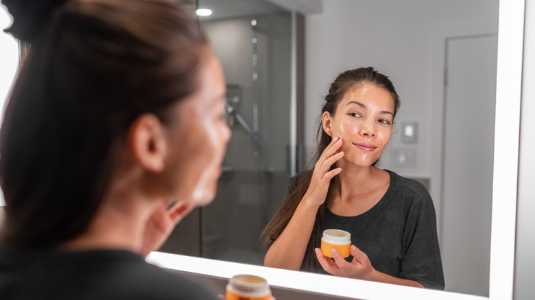 Woman looking in mirror putting on skincare