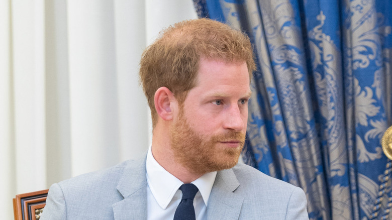 Prince Harry straight-faced while wearing a light gray suit with a dark blue tie