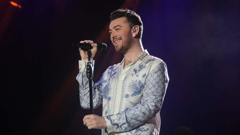 Sam Smith holding a microphone stand and smiling