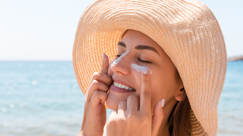 Woman applying sunscreen to nose and undereyes on beach