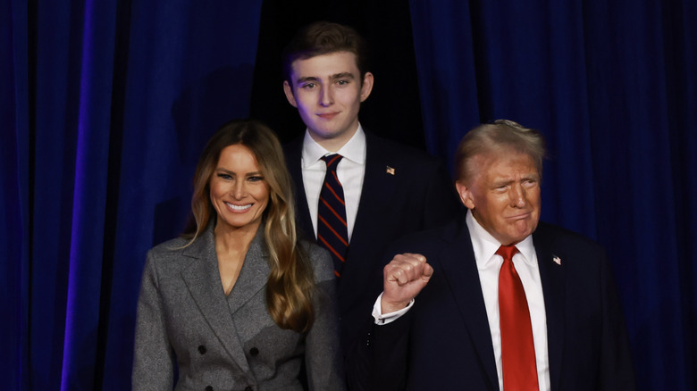 Barron Trump standing behind his parents In a navy suit