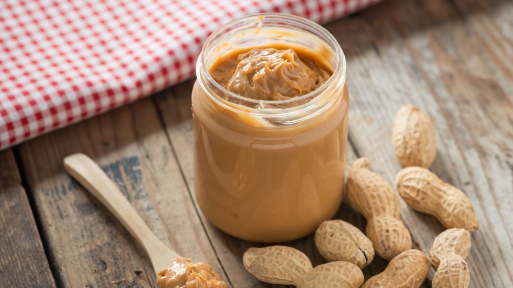 A jar of peanut butter with peanuts on a table, a favorite snack of Christina Anstead's