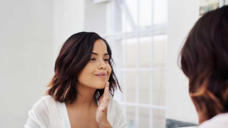 woman gazing into mirror, touching face