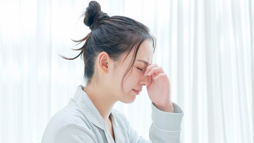 A woman with closed eyes touching her head 