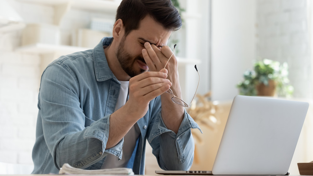 Man seated at computer rubbing his eyes.