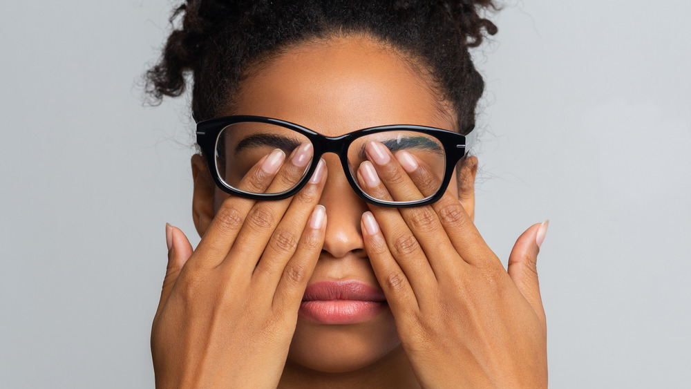 Woman wearing black glasses rubs her eyes