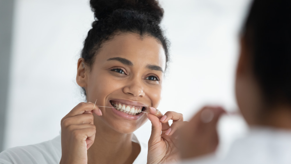 Woman looking in mirror flossing.