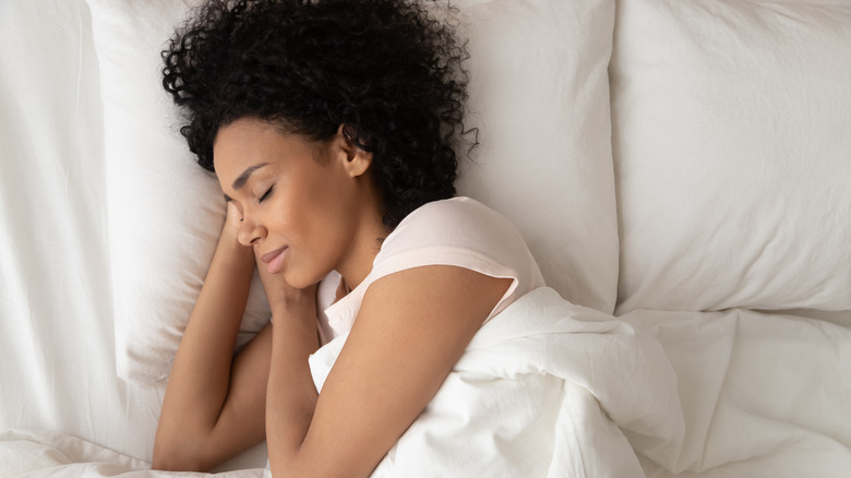 Woman wearing white sleeping peacefully with her head on a white pillow.