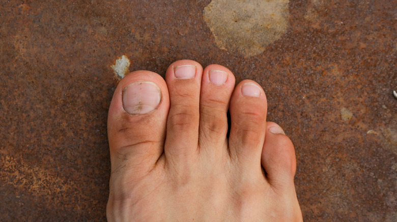 Foot with a small pinky toe on brown floor