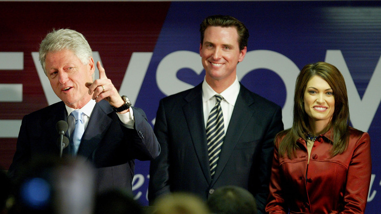 Gavin Newsom and Kimberly Guilfoyle smiling behind Bill Clinton