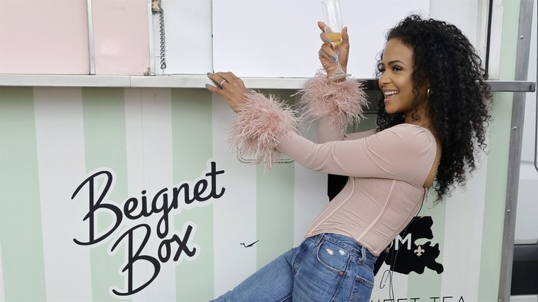 Christina Milian holding champagne flute by Beignet Box sign