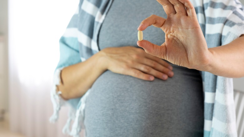 A pregnant person holding a pill