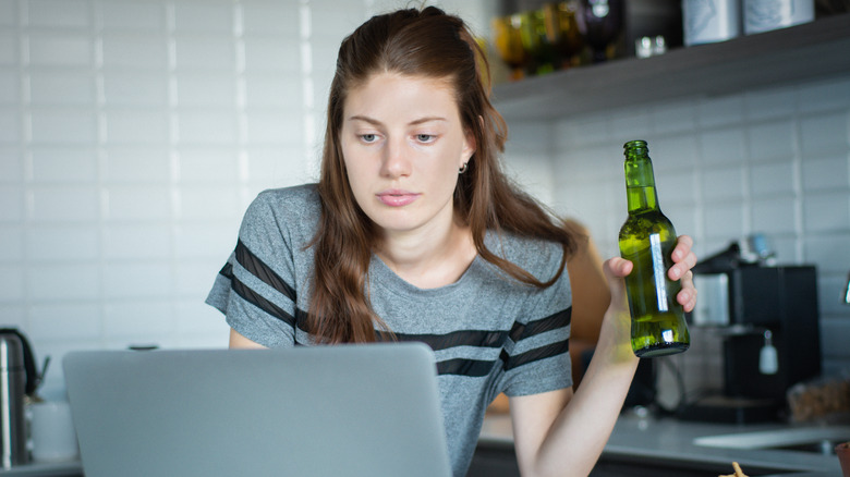 Woman holding a beer while on laptop