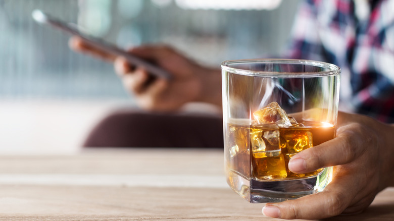 Person drinking whiskey while looking at the phone