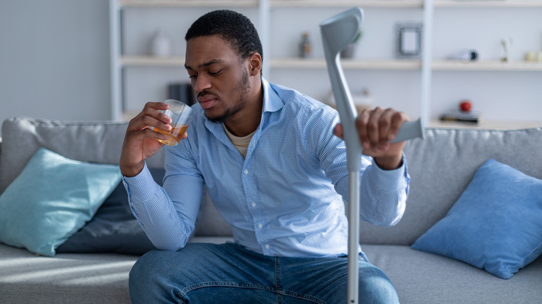 man holding crutch and whiskey