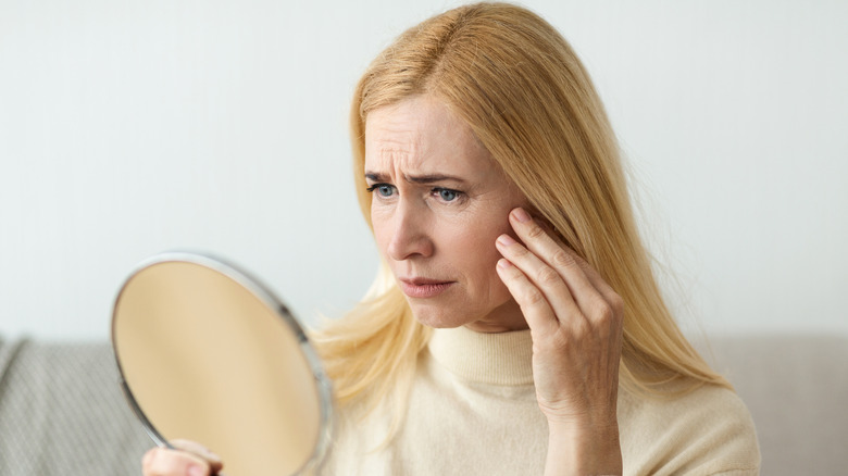 A blonde woman looking in the mirror, concerned