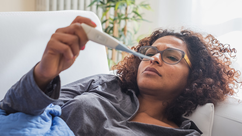 A woman laying down taking her temperature