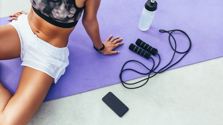 Woman seated next to jump rope, cell phone, and water bottle