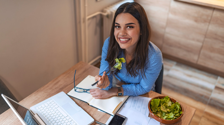 A woman eating salad and working