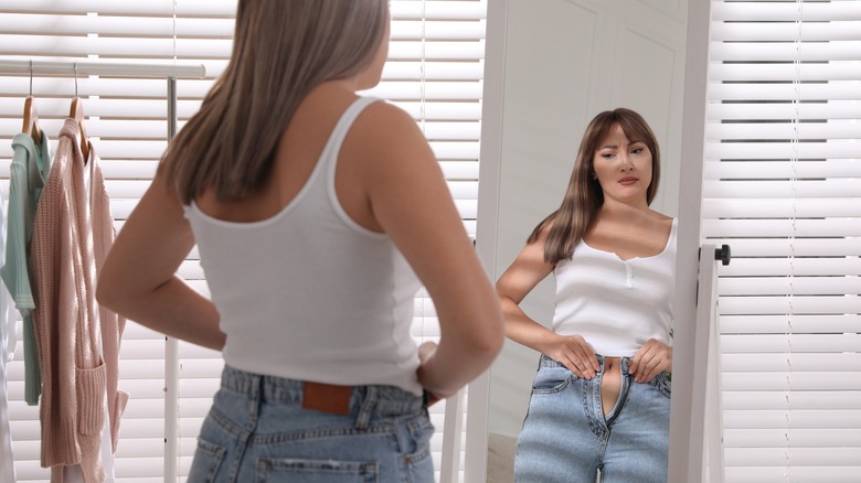 Woman fastening jeans in mirror