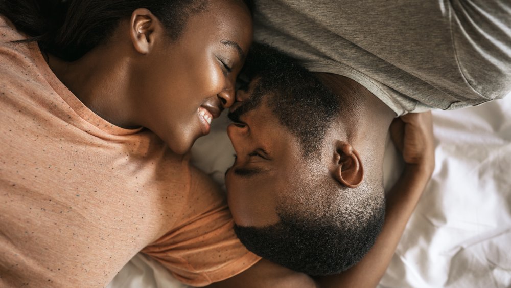 A man and a woman in bed, about to kiss