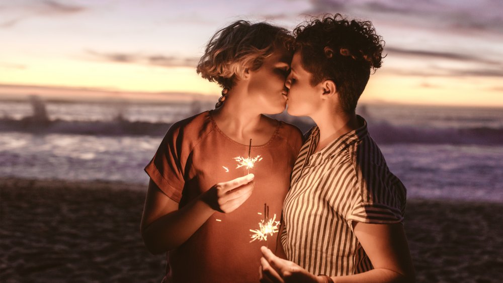 Two women kissing on the beach, holding sparklers