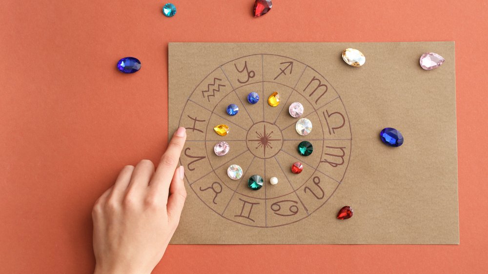 hand moving birth stones over a zodiac chart