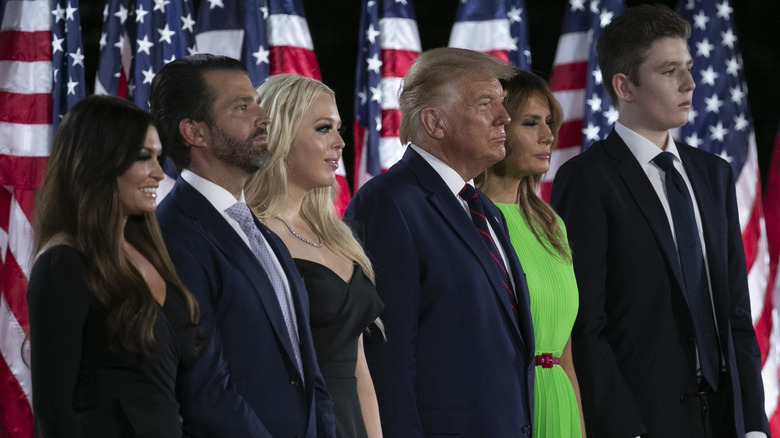 Kimberly Guilfoyle, Donald Trump Jr., Tiffany Trump, Donald Trump, Melania Trump, and Barron Trump ose in front of American flags.