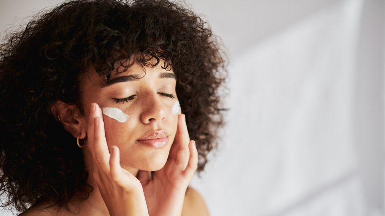 Woman with curly hair applying ointment to face