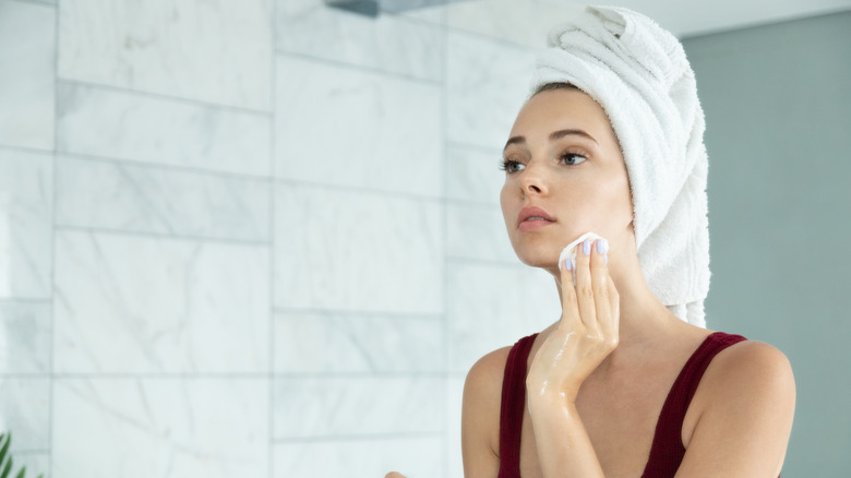 A woman with a towel on her hair washes her face.