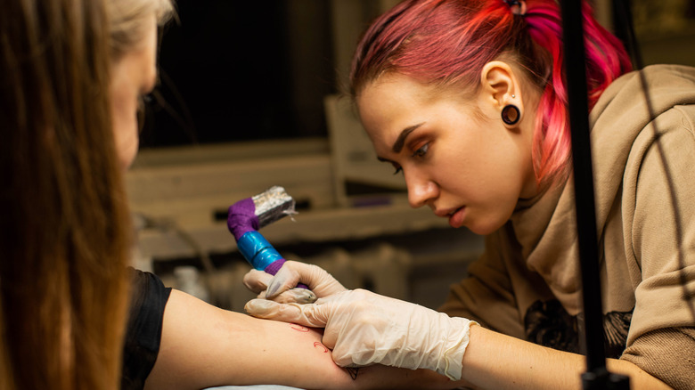 A tattoo artist tattoos a client