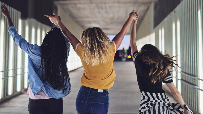 Three friends hold hands and walk together