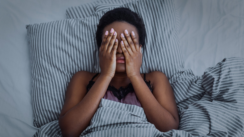 Woman covering her face while lying in bed