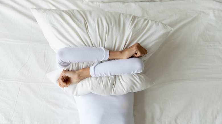 Woman laying in bed covering her face with a pillow 